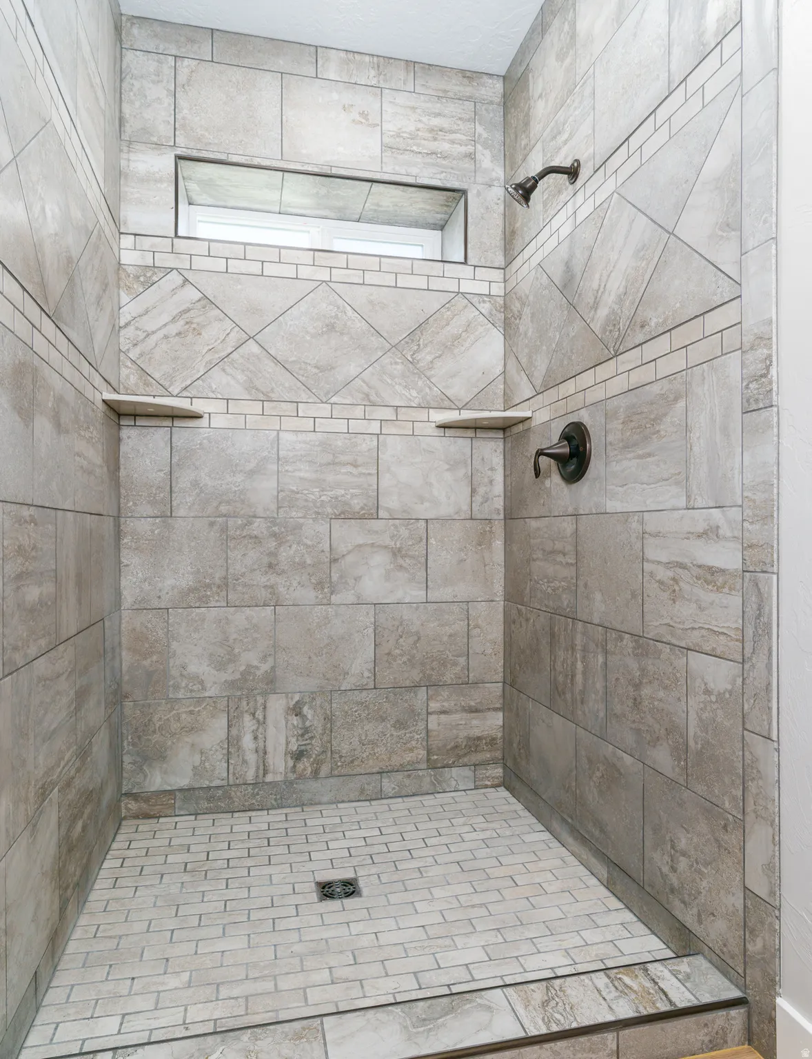 Tiled shower featuring a recessed niche, dual built-in shelves, and a bronze shower fixture