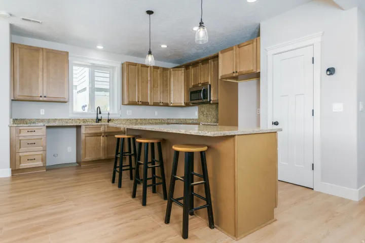 Wood-finish flooring, L-shaped kitchen counter with integrated sink, stainless steel microwave, light wood cabinetry, and recessed lighting