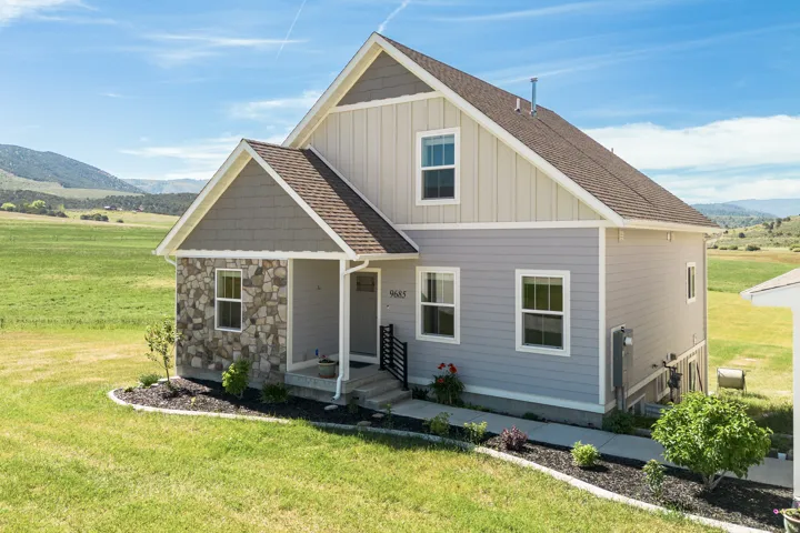 Stone and siding exterior with a covered entry, gabled rooflines, and a manicured front lawn with plantings