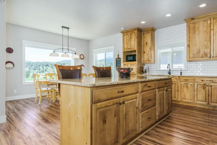 Kitchen featuring wood-finish flooring, natural wood cabinetry, white subway tile backsplash, and a large central island with a stone countertop