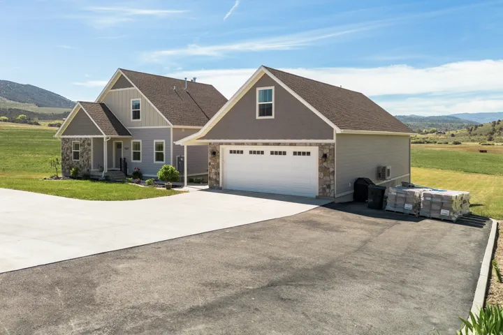 Two-story residence featuring light gray siding, stone accents, a covered front porch, and an attached two-car garage