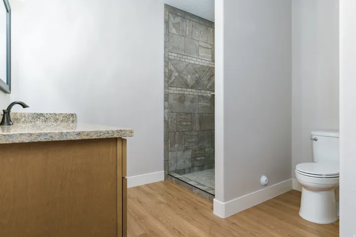 Wood-finish flooring, vanity with stone countertop, dark bronze faucet, and a tiled shower with glass enclosure