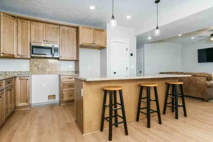 Kitchen featuring light wood cabinetry, stone countertops, stainless steel microwave, and wood-finish flooring