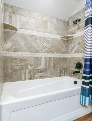 White bathtub with a bronze showerhead and fixture, set against a tiled wall featuring a decorative accent band and two corner shelves