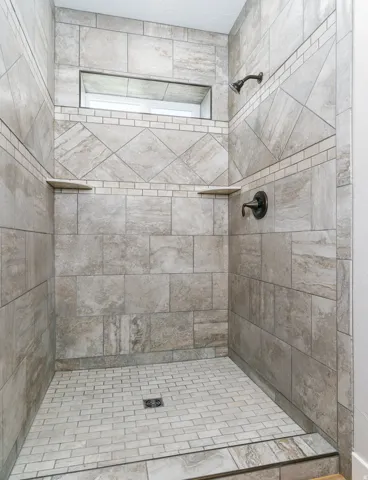 Tiled shower featuring a recessed niche, dual built-in shelves, and a bronze shower fixture