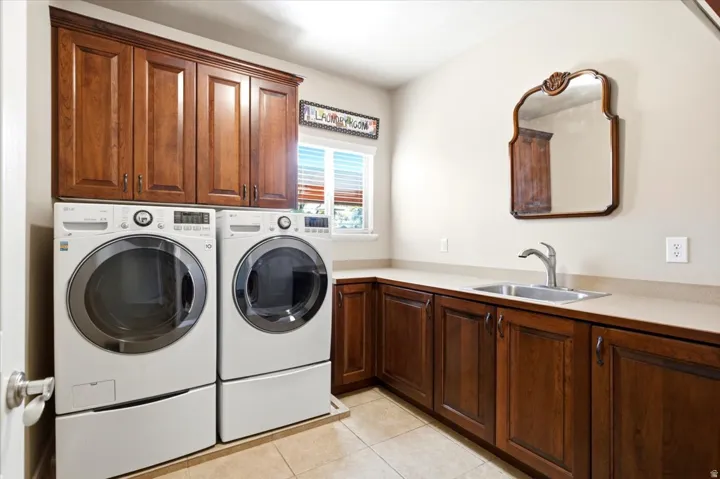 Laundry area featuring wood cabinetry, a utility sink, light-toned countertops, and tile flooring