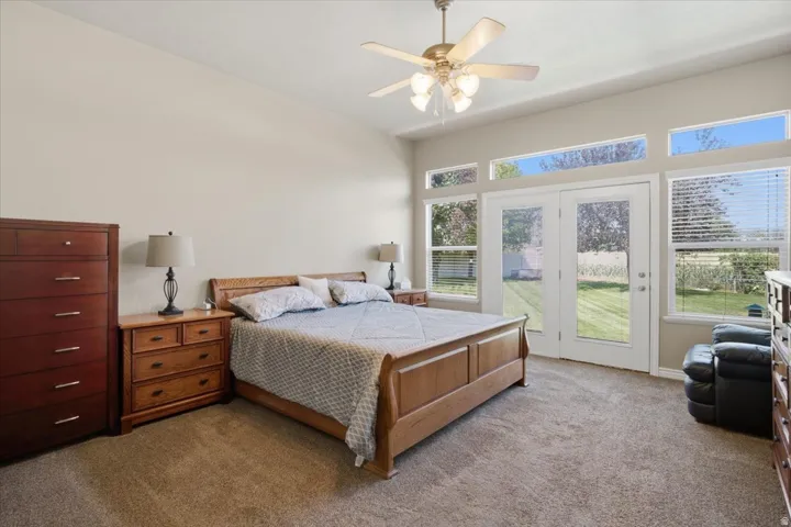 Vaulted ceiling with ceiling fan, dual French doors with transom windows, additional transom windows, and carpeted flooring