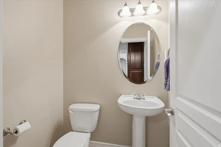 Pedestal sink with chrome fixtures, oval mirror, and three-light vanity fixture
