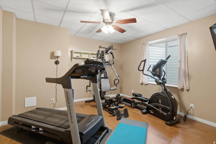Room featuring wood-finish flooring, a drop ceiling, and a ceiling fan with light fixture