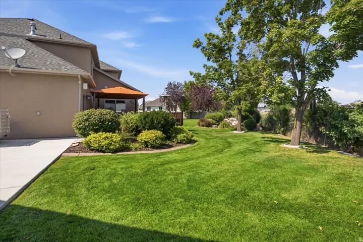 Expansive green lawn, mature trees, landscaped shrubbery, concrete patio, and a covered outdoor area
