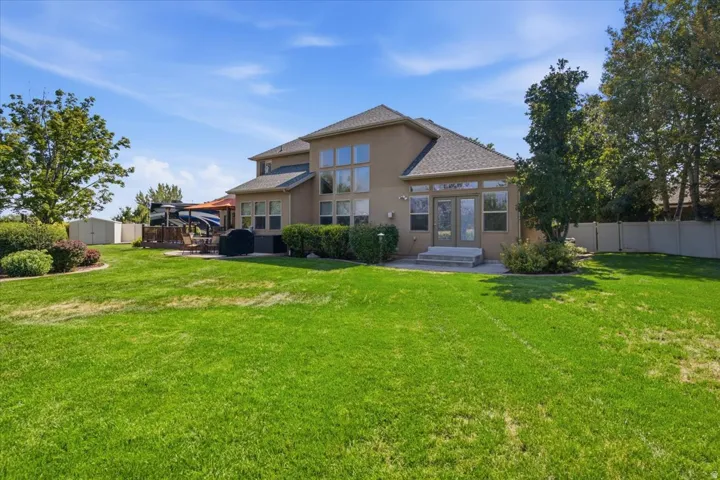 Expansive green lawn, stucco exterior, multi-pane windows, and a raised wood-finish deck with a pergola