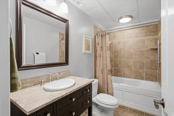 Bathroom featuring a dark wood finish vanity with a countertop basin sink, a stone-finish countertop, a large framed mirror, and a tiled shower-over-tub combination with a grab bar