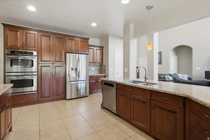 Spacious kitchen featuring extensive wood cabinetry, stainless steel appliances, a large center island with a double basin sink, light-toned countertop, and tile flooring