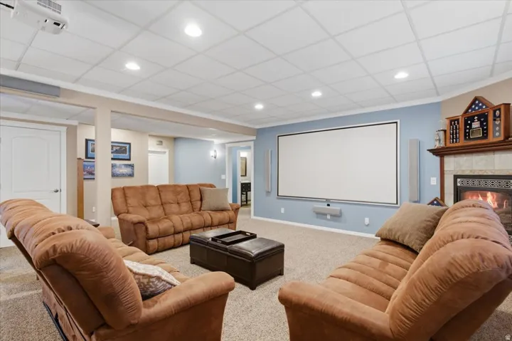 Recessed lighting, drop ceiling, wall-mounted projection screen, built-in fireplace with tile surround, and wood mantel