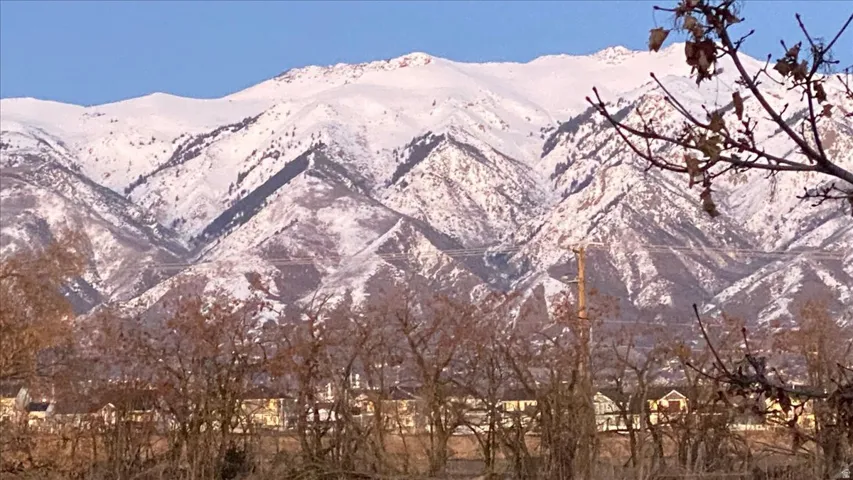 Snow-capped mountain range with scattered trees and residential structures in the foreground