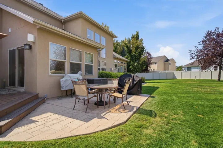Expansive green lawn, paver patio, composite deck with steps, stucco exterior, and multiple windows