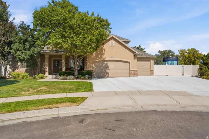 Stucco exterior with stone accents, two-car garage, covered entry with columns, concrete driveway, and established landscaping