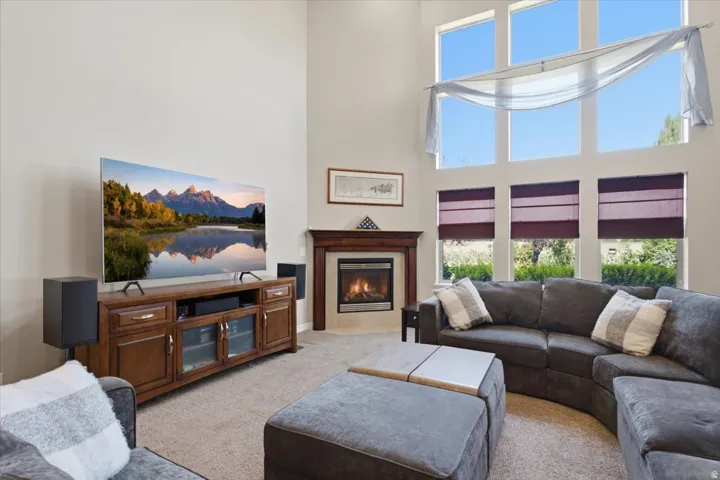 Vaulted ceiling with multiple upper windows, corner fireplace with wood mantle, and wall-to-wall carpeting