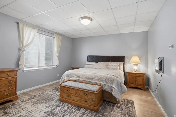 Neutral wall paint, wood-finish flooring, drop ceiling, and a window with blinds