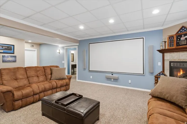 Built-in media screen with integrated speakers, recessed lighting, carpeted flooring, and a fireplace with a tile surround and wood mantle