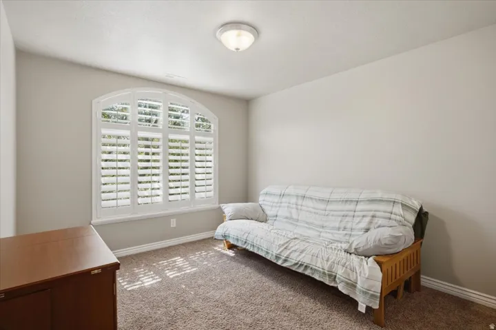 Arched window with plantation shutters, neutral wall color, and textured carpeting