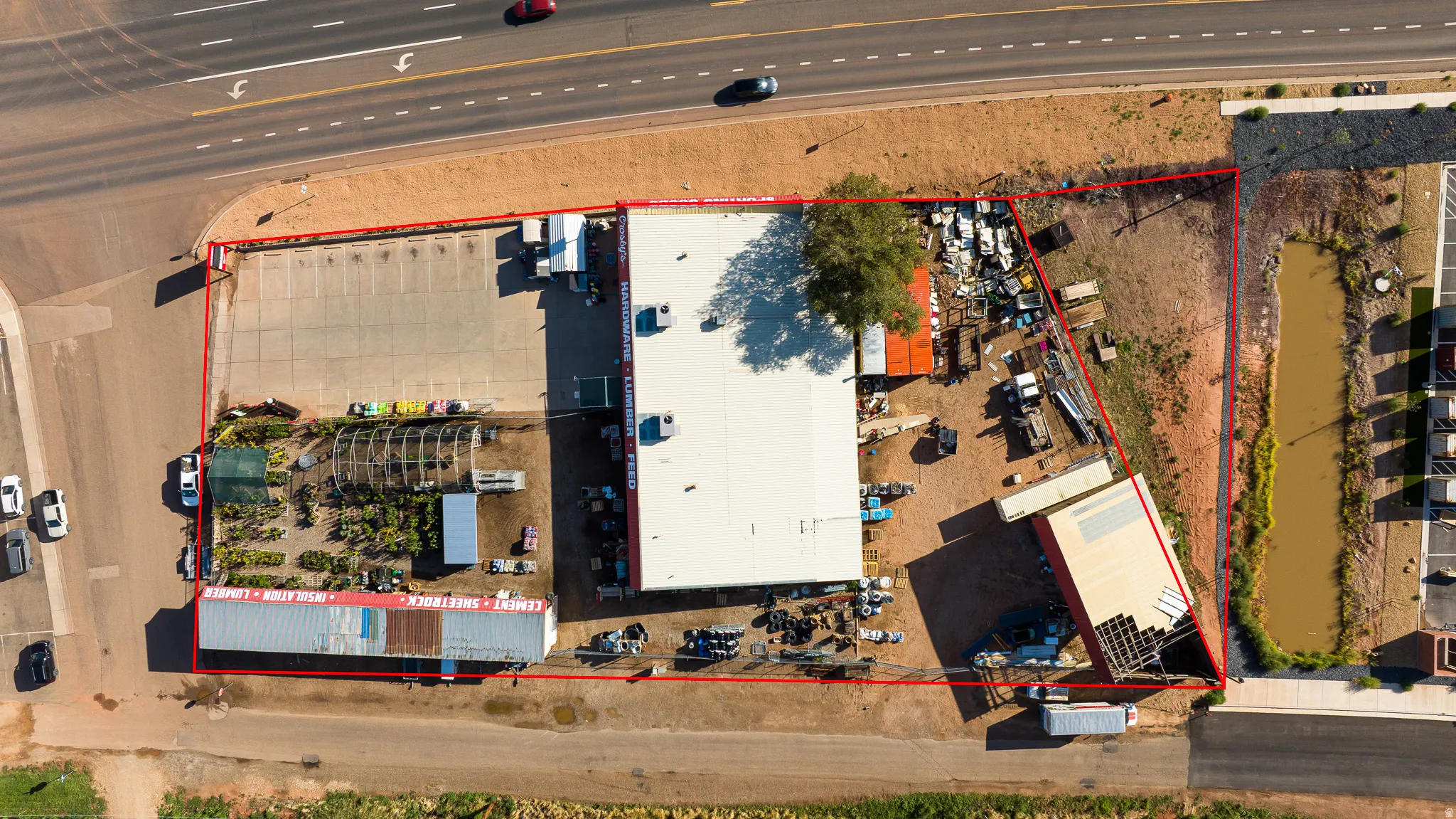 Expansive commercial property featuring multiple structures, a large paved parking area, a greenhouse, and a natural water feature