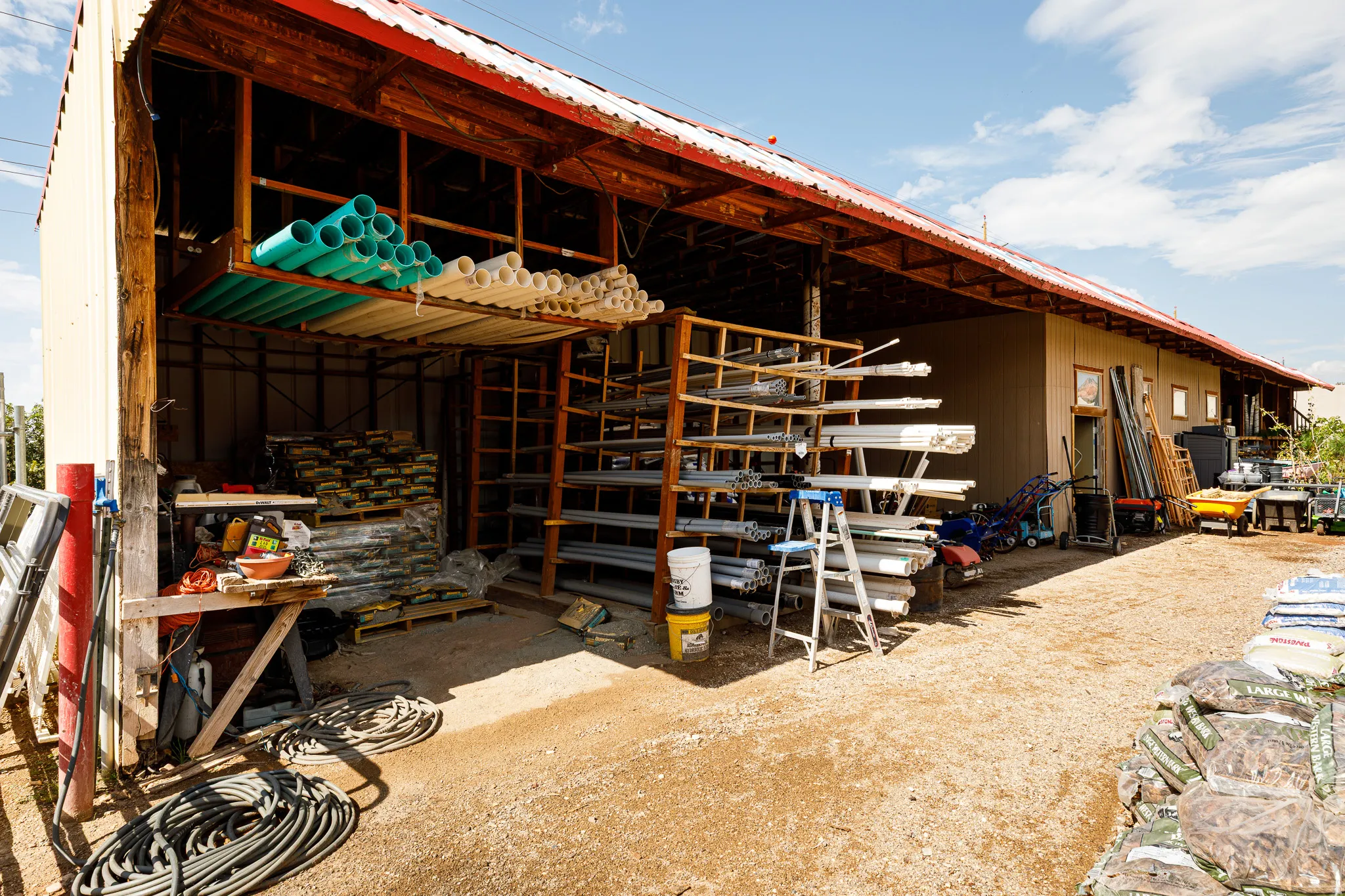 Open-sided storage structure featuring a red corrugated metal roof and exposed wood beams