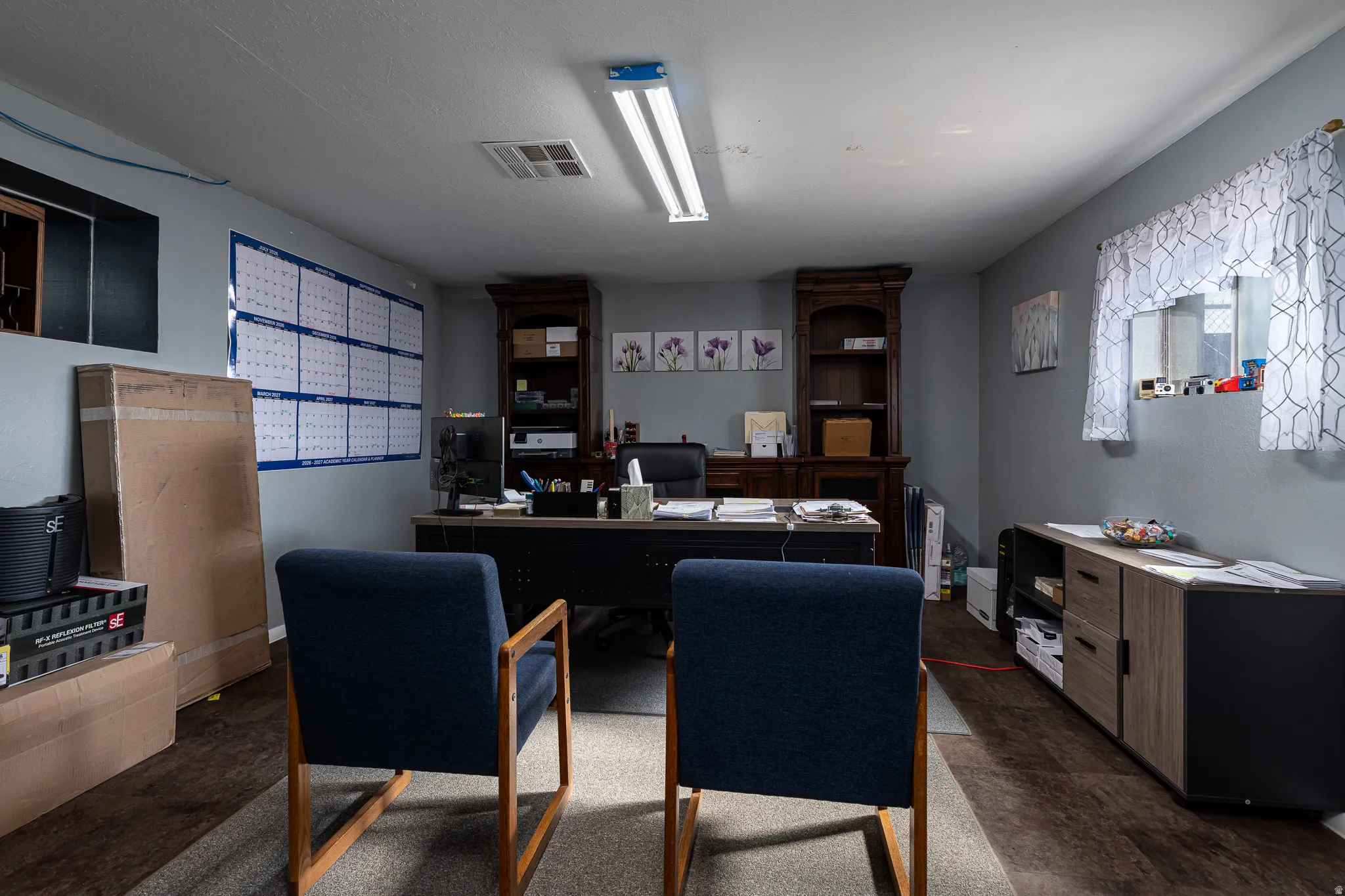 Dedicated office space with wood-finish flooring, two windows, and built-in shelving units