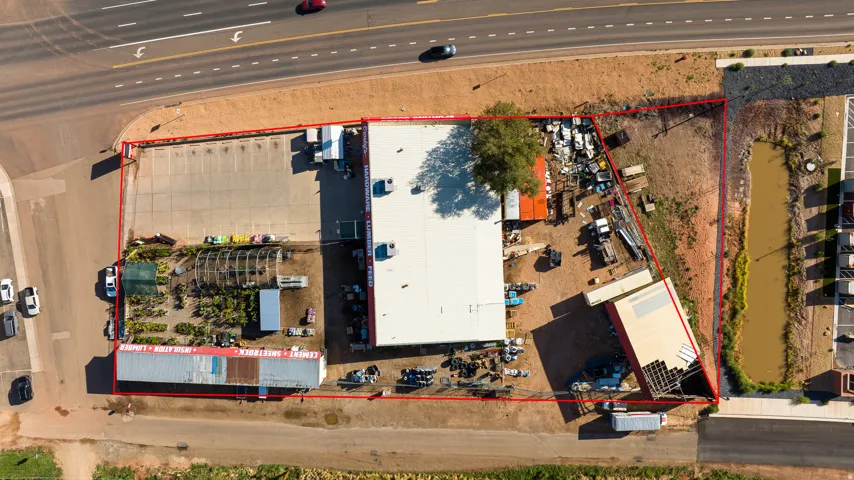 Expansive commercial property featuring multiple structures, a large paved parking area, a greenhouse, and a natural water feature