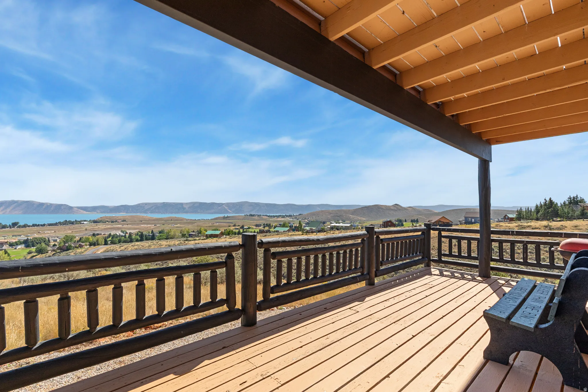 Spacious covered deck featuring wood-finish flooring, wood railings, and expansive mountain and lake scenery