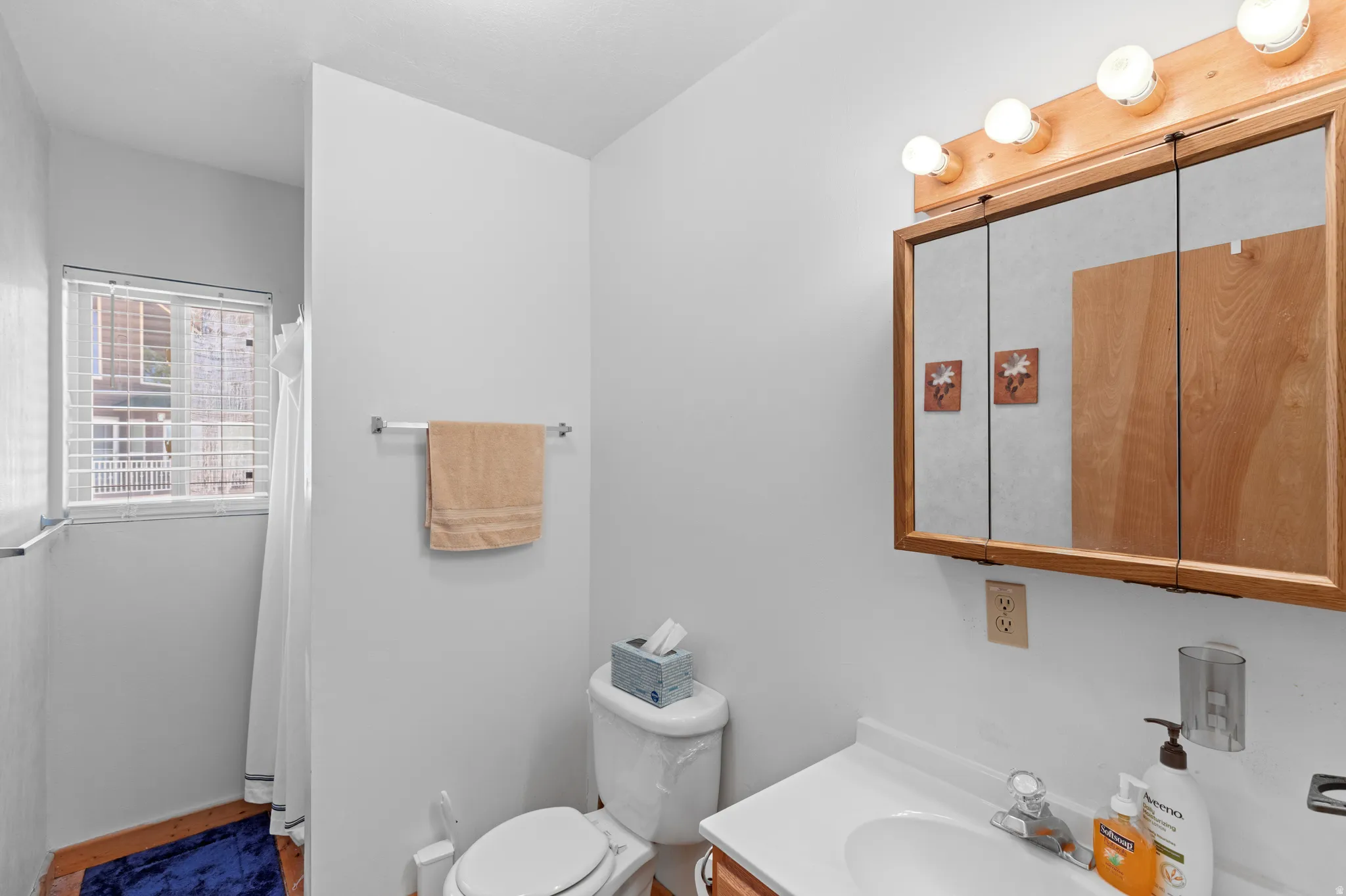 White vanity with integrated sink, wood-finish medicine cabinet with mirror, and three-bulb vanity lighting