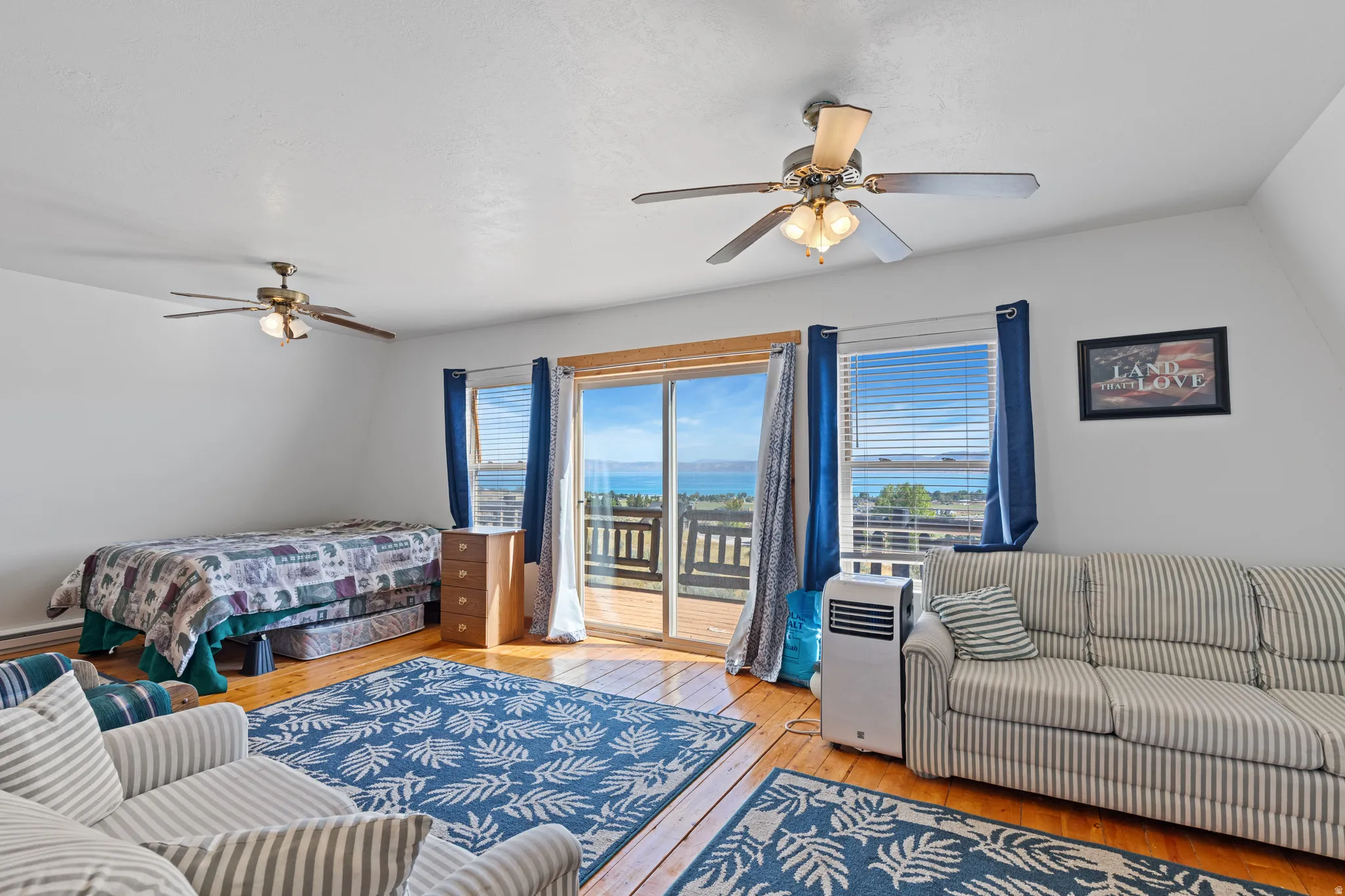 Hardwood flooring, dual ceiling fans with light kits, sliding glass door with balcony access, and two windows providing expansive water scenery