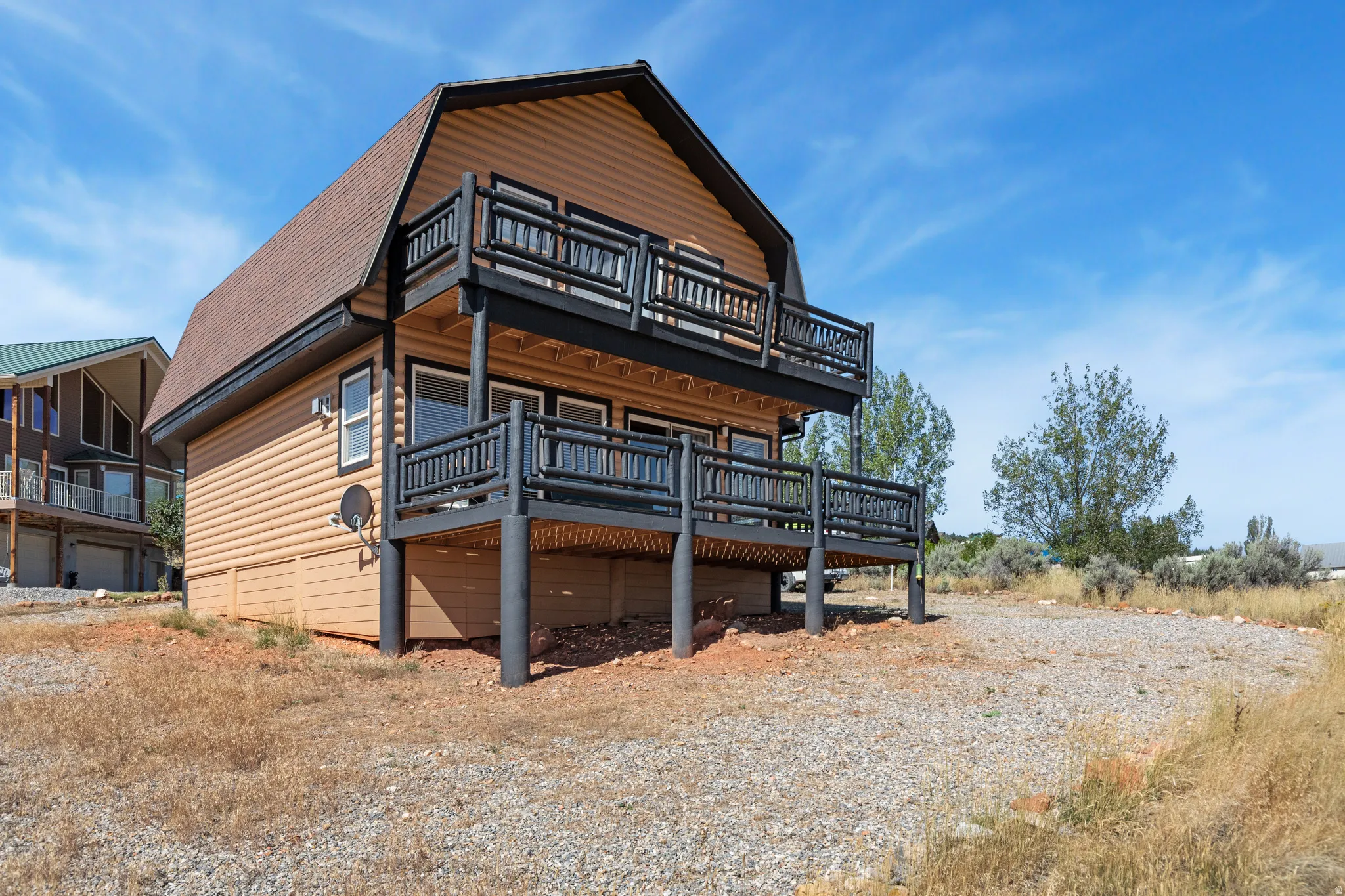 Barn-style architecture featuring light wood-finish siding, a dark shingle roof, and a gravel surface