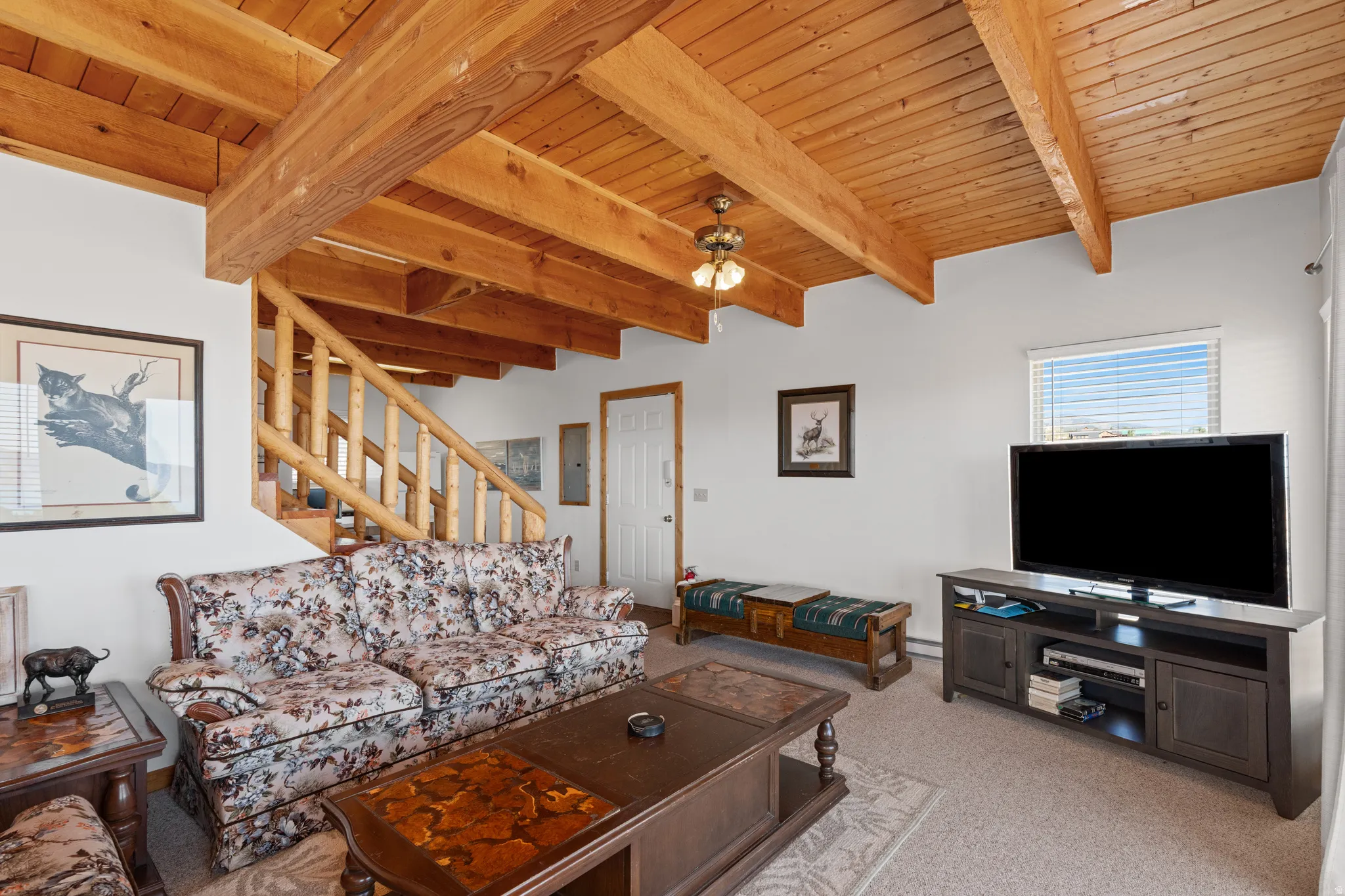 Vaulted wood-paneled ceiling with exposed beams, wood staircase with log railing, and carpeted flooring