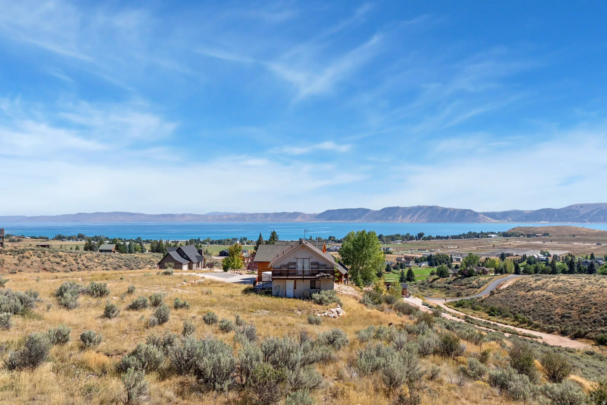 Expansive property with a wood-sided exterior, wrap-around deck, and visible lake and mountain scenery