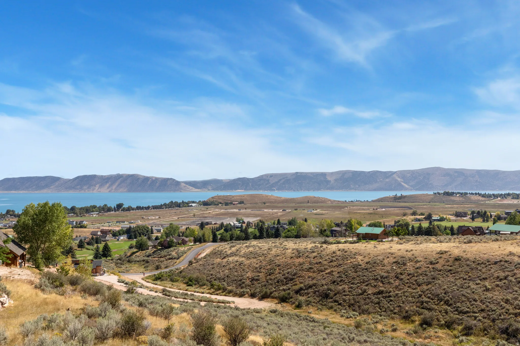 Expansive natural landscape with a prominent body of water, distant mountains, and scattered residential structures