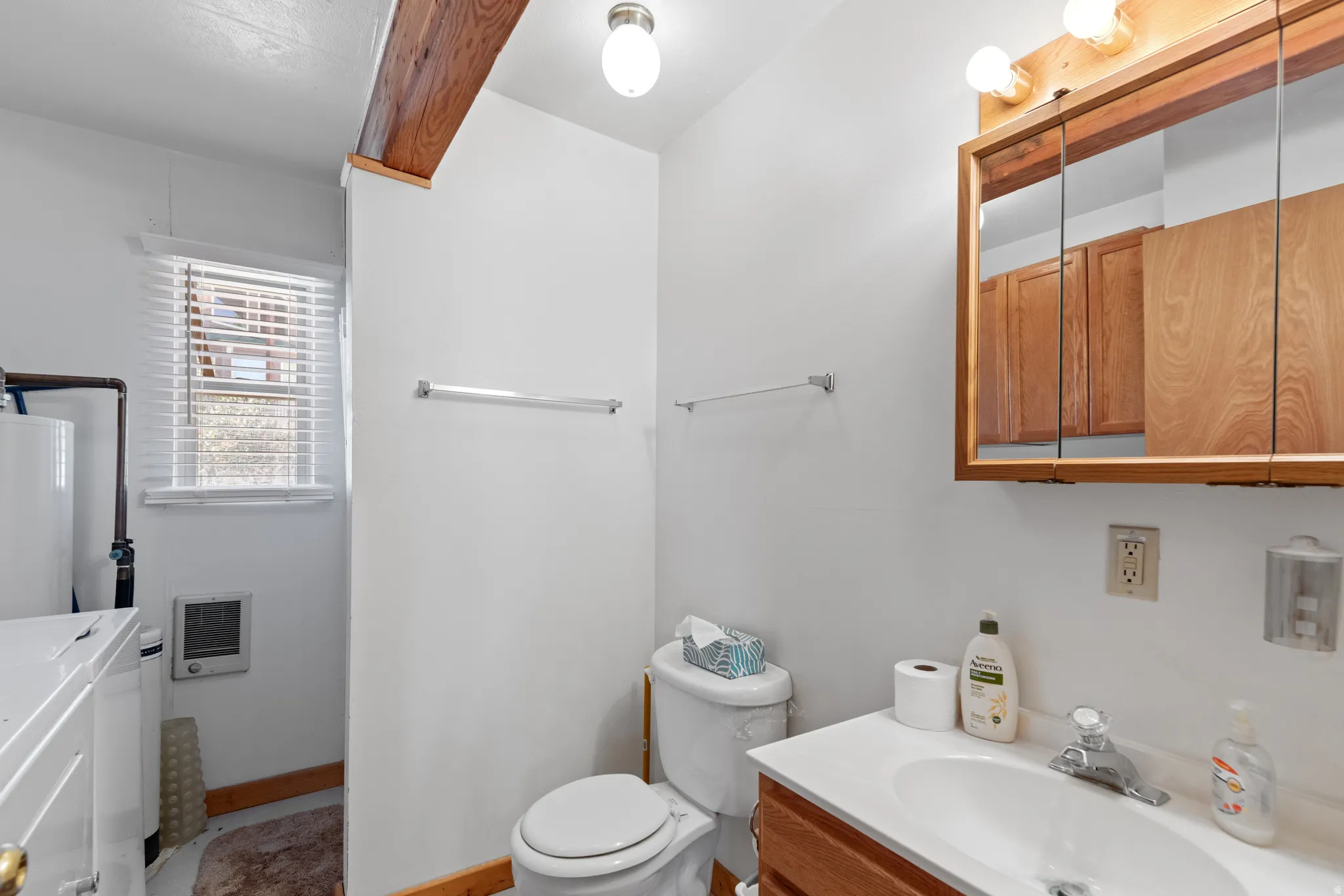 Bright bathroom featuring a white subway tile surround, wood-finish vanity with dual sink basins, mirrored medicine cabinet with wood-frame trim, and natural light from a window