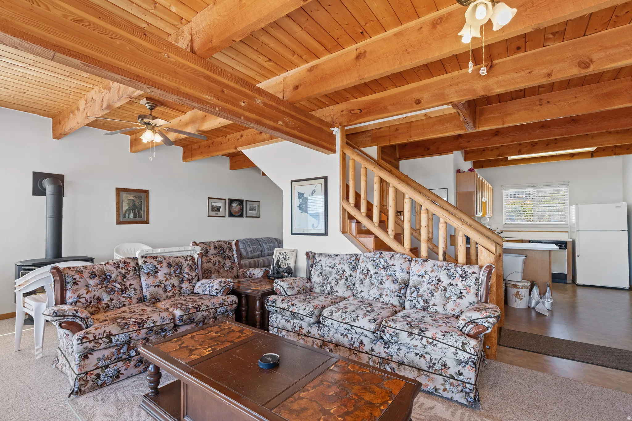 Wood-finish ceiling beams, ceiling fans with integrated lighting, wood-finish staircase with balusters, freestanding wood-burning stove, and a built-in refrigerator
