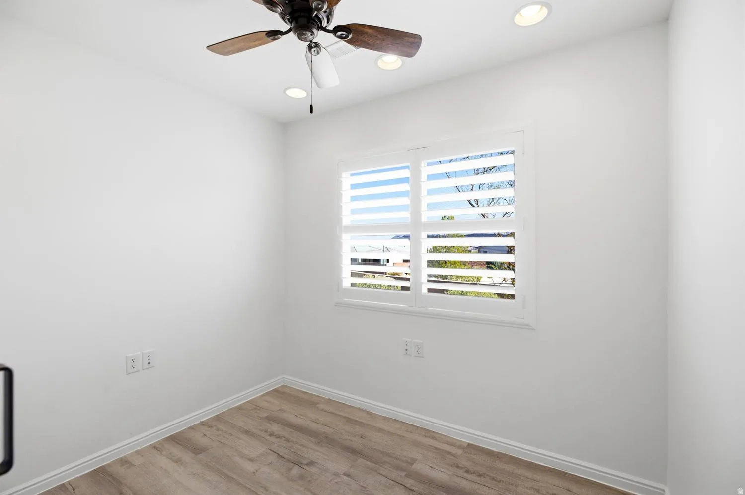 Bright secondary bedroom showcasing wood-finish flooring, white walls, and dual casement windows with horizontal shutters providing natural light and ventilation