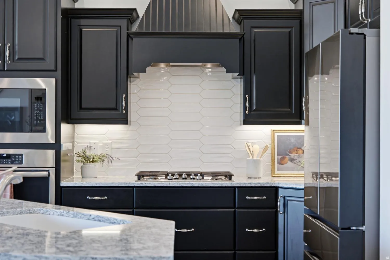 Dark wood cabinetry with crown molding, stainless steel appliances, light-toned tiled backsplash, recessed under-cabinet lighting, and light-toned countertop with integrated sink