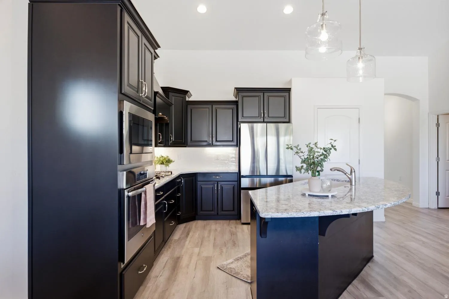 Black cabinetry with stainless steel appliances, granite island countertop, wood-finish flooring, and recessed lighting