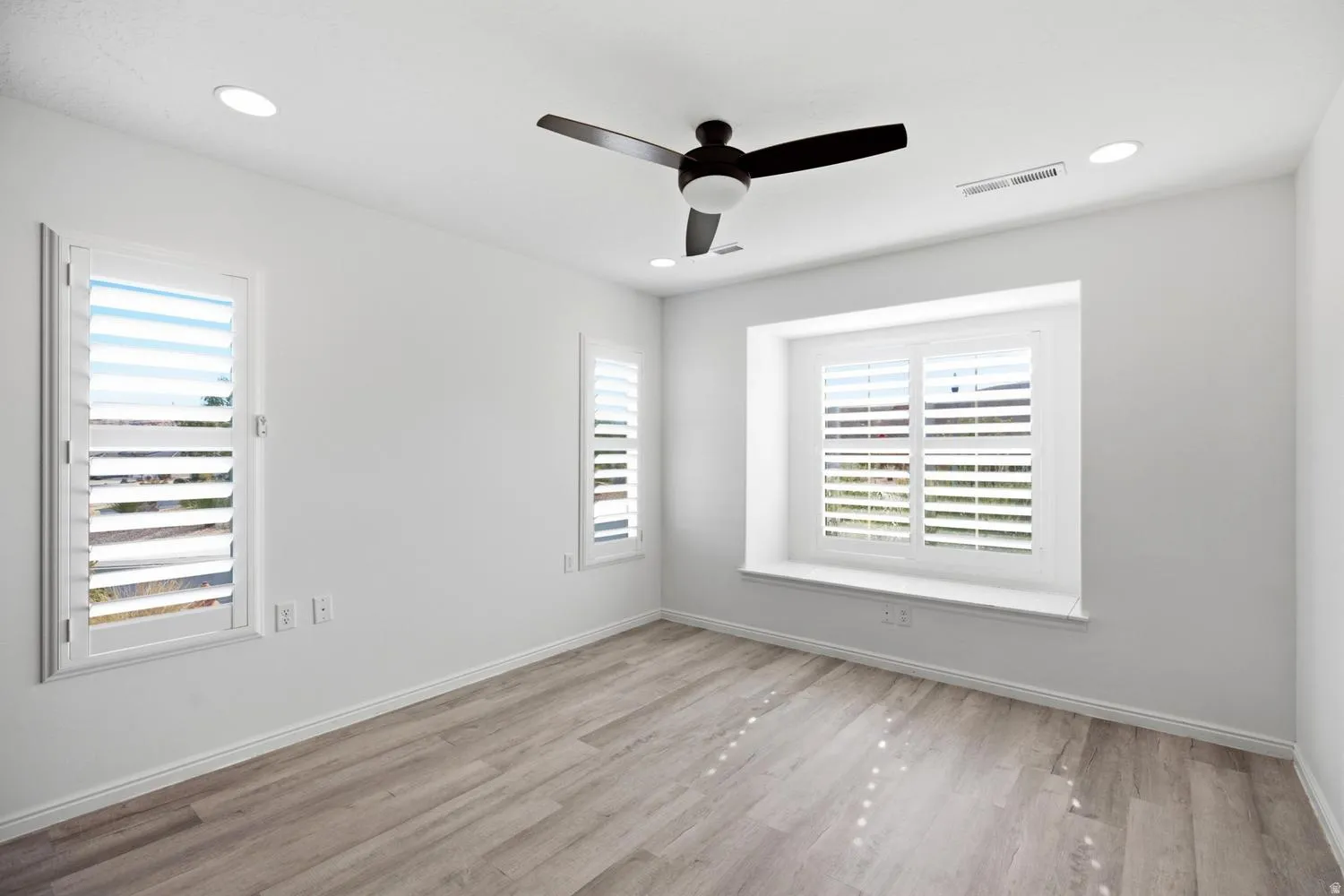 Recessed ceiling lighting, a ceiling fan with integrated lighting, wood-finish flooring, and multiple windows with plantation shutters