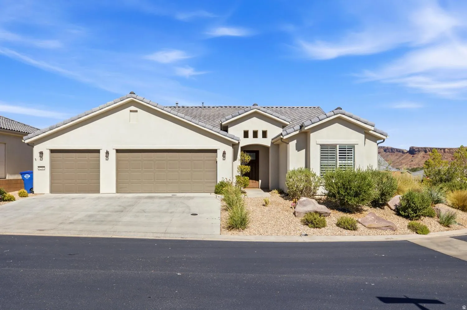 Stucco exterior with a tiled roof, two-car garage, and desert-style landscaping