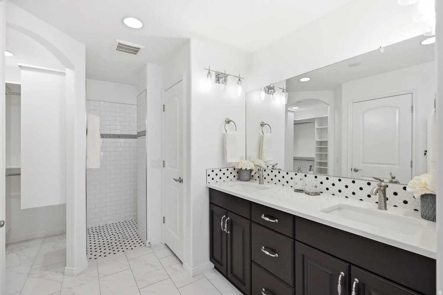 Spa-inspired primary bathroom featuring a dual-sink vanity with black cabinetry, white quartz countertop, and polished chrome hardware