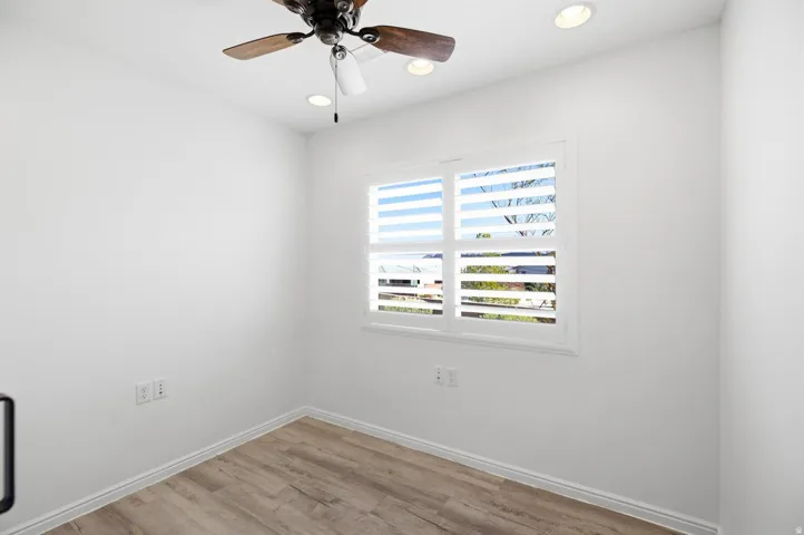 Bright secondary bedroom showcasing wood-finish flooring, white walls, and dual casement windows with horizontal shutters providing natural light and ventilation