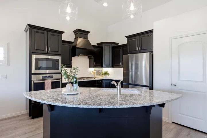 Kitchen featuring dark cabinetry, stainless steel appliances, a built-in microwave and oven, a white tile backsplash, and an island with a light-colored countertop and undermount sink