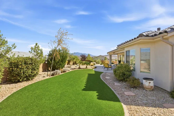 Expansive backyard featuring artificial turf, a stone-lined pathway, and a covered patio with concrete flooring
