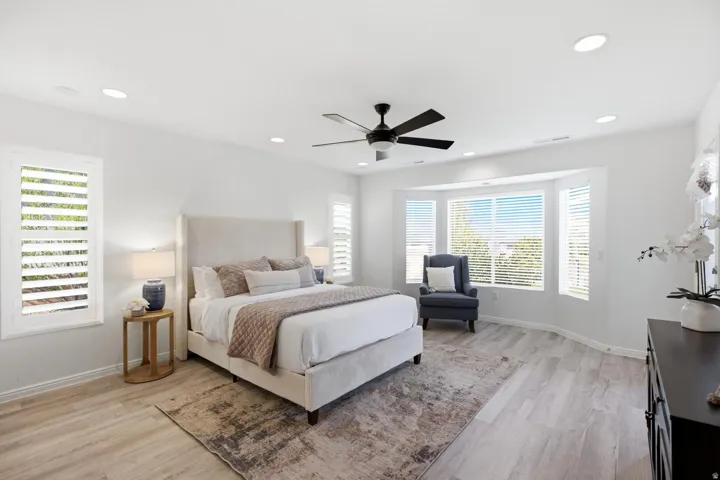 Recessed lighting, ceiling fan, bay window, wood-finish flooring, and white plantation shutters