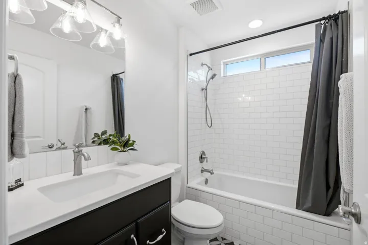 Bathroom featuring a white subway tile surround, built-in bathtub, dual-flush toilet, and black vanity with a white countertop and integrated sink