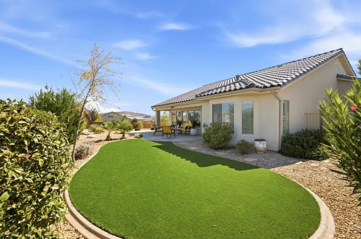 Beautifully landscaped backyard featuring a curved synthetic turf lawn with integrated hardscape edging, mature hedging along the perimeter, and drought-resistant plantings